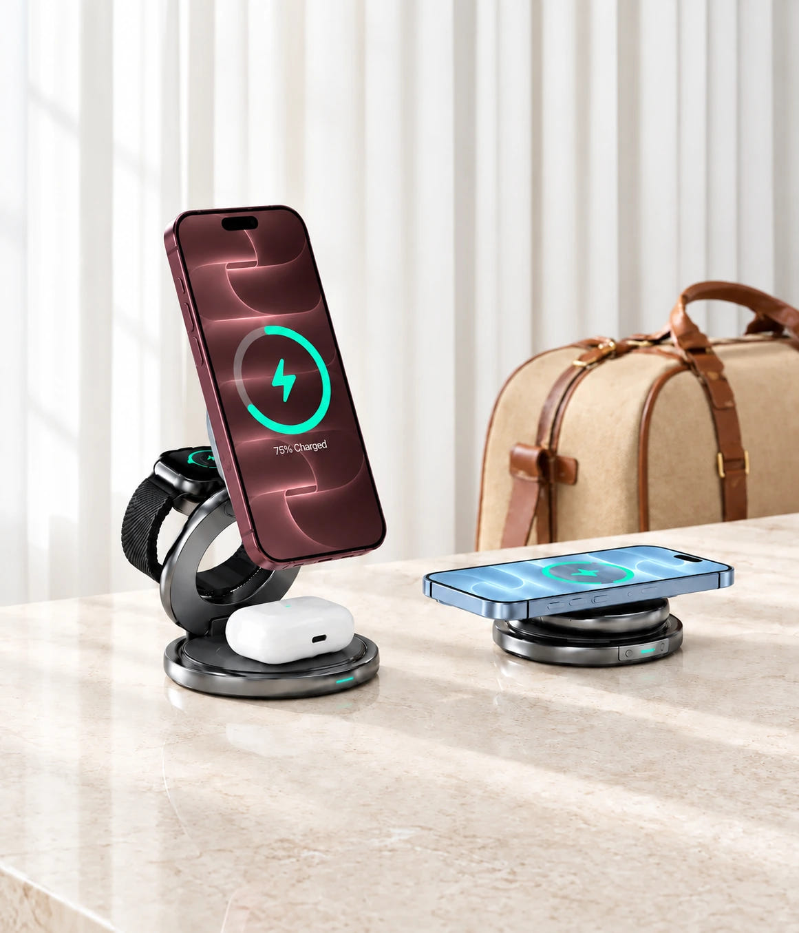 Two folding wireless charging stations with phones, watch and earbuds beside a travel bag in a bright room.