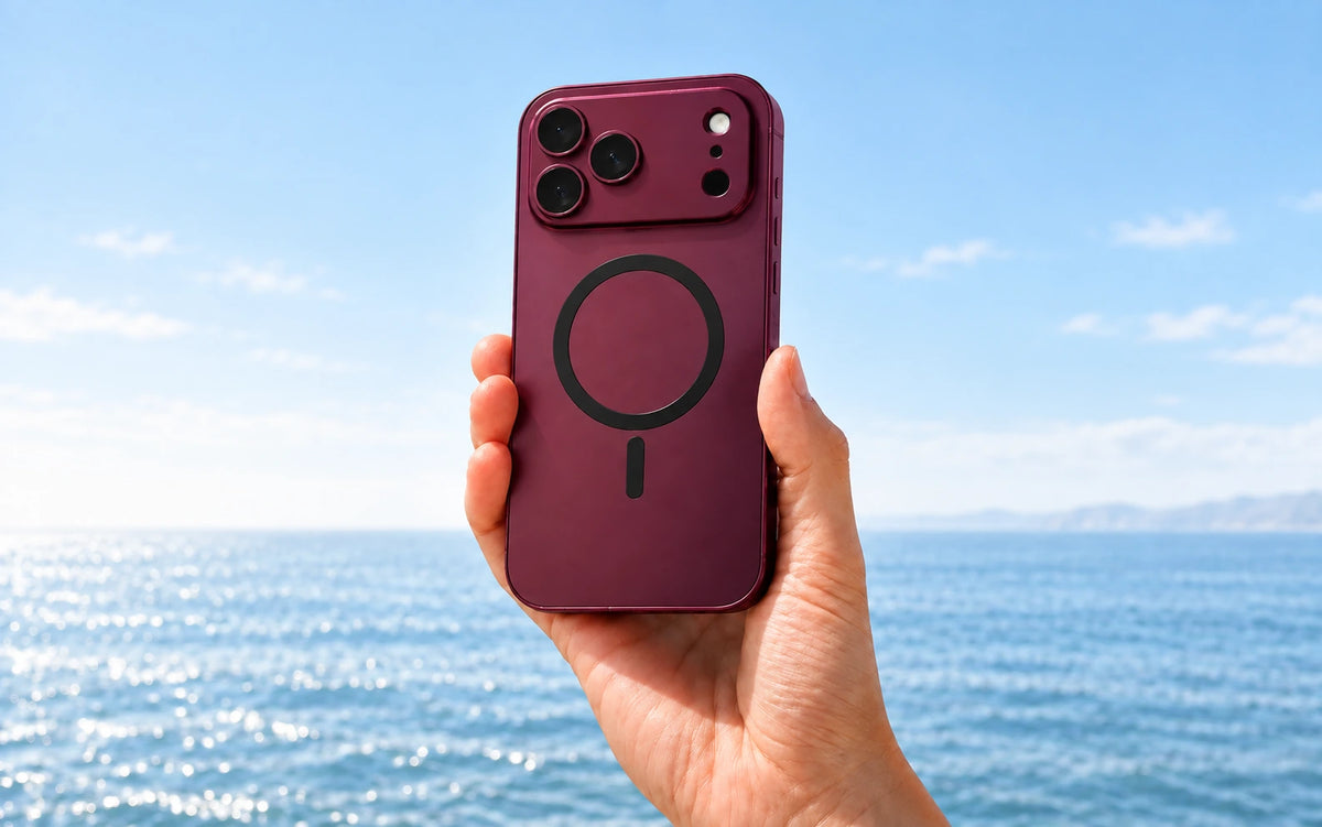 Hand holding a Burgundy magnetic phone case against a softly lit blue sea.